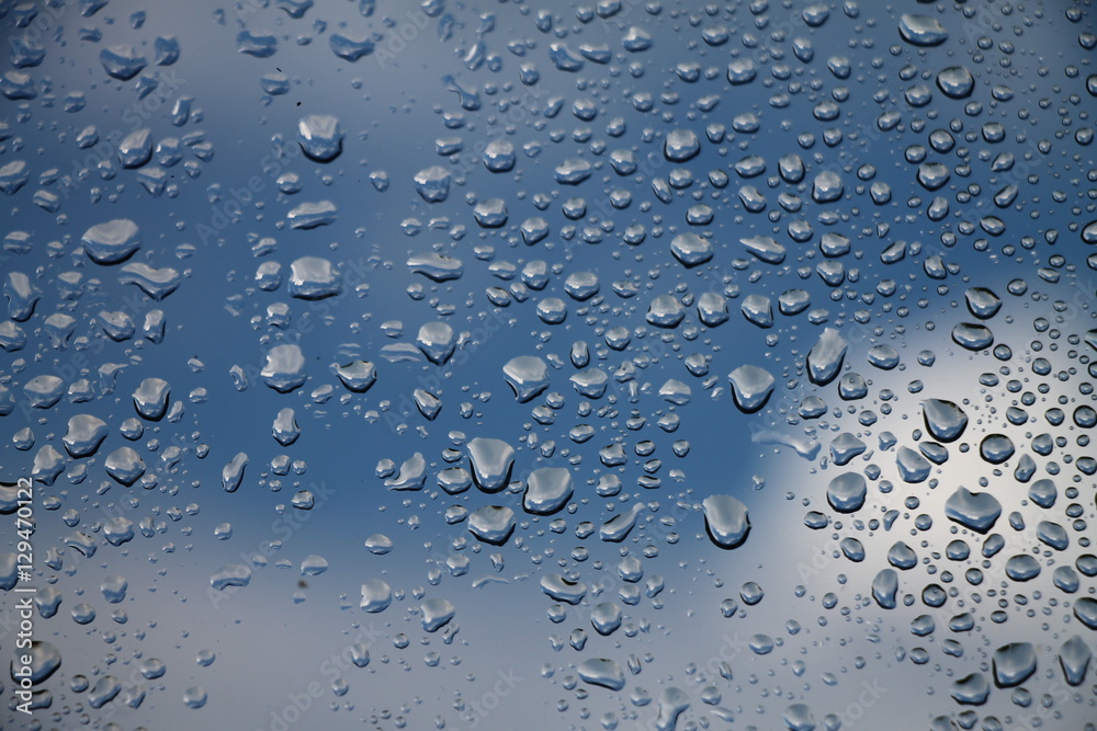 Rain drops on window with blue cloudy sky in background , spring rainy day
