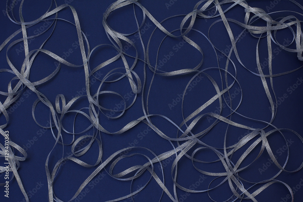 Silver ribbon in the form of waves and curls on a dark blue background. Christmas/New year decor. Silver ribbon in the form of waves and curls on a dark blue background. Christmas/New year decor.