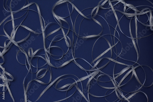 Silver ribbon in the form of waves and curls on a dark blue background. Christmas/New year decor.