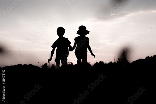 Silhouettes of kids jumping off a cliff at sunset. Little boy and girl jump high holding hands. Brother and sister having fun in summer. Friendship  freedom concept. 