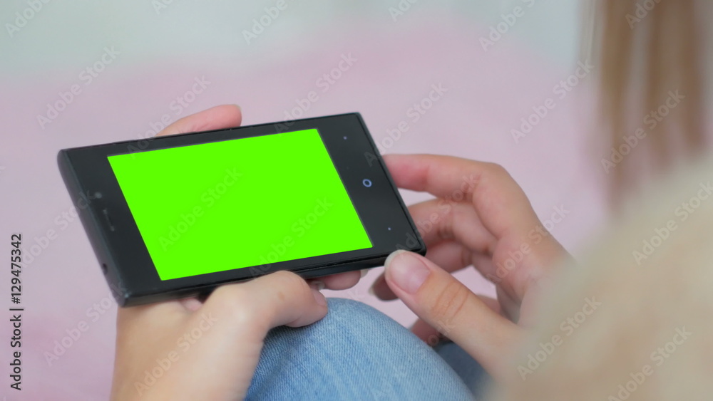 Woman looking at horizontal smartphone with green screen. Close up shot of woman's hands with mobile