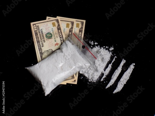 Cocaine drug powder bag on dollar money bills, cocaine pile and lines on black background