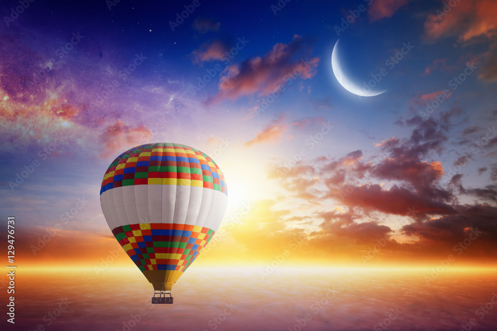 Obraz premium Hot air balloon rises very high in sunset sky above glowing clou