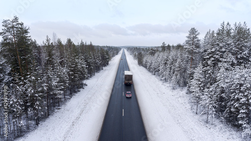Small car driving next to semitrailer truck on winter asphalt road. The Kola route is in northern part of Karelia, Russia. Aerial view from drone