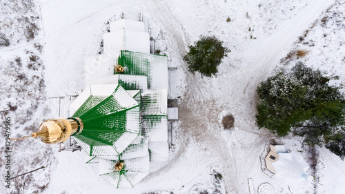 Aerial view at the green domes of wooden church covered with snow at winter. Golden cross is on the top. © Kekyalyaynen