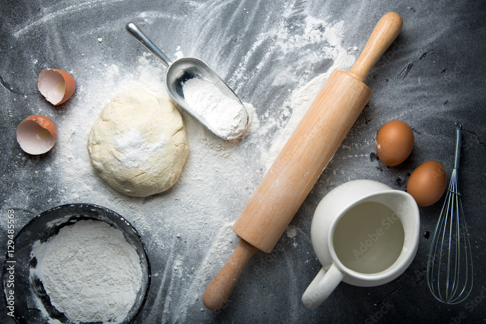 Baking cake ingredients. Bowl, flour, eggs, egg whites foam, egg beater, rolling pin and eggshells on black chalkboard Baking cake ingredients. Bowl, flour, eggs, egg whites foam, egg beater, rolling pin and eggshells on black chalkboard