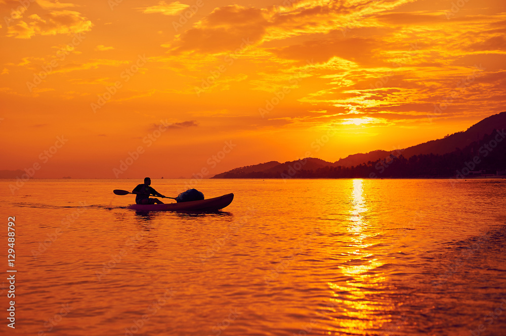Beautiful sunset. Man swimming on a boat in the sea