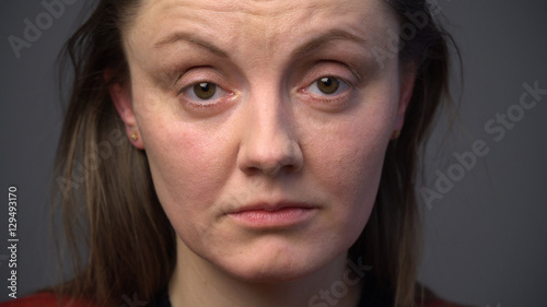 Close up sad adult woman's face against gray background