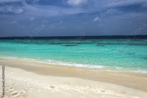 Typically Maldivian Landscape shot on a cloudy day with turquoise ocean  blue sky and white sandy beach. An amazing color combination of three tones of blue.