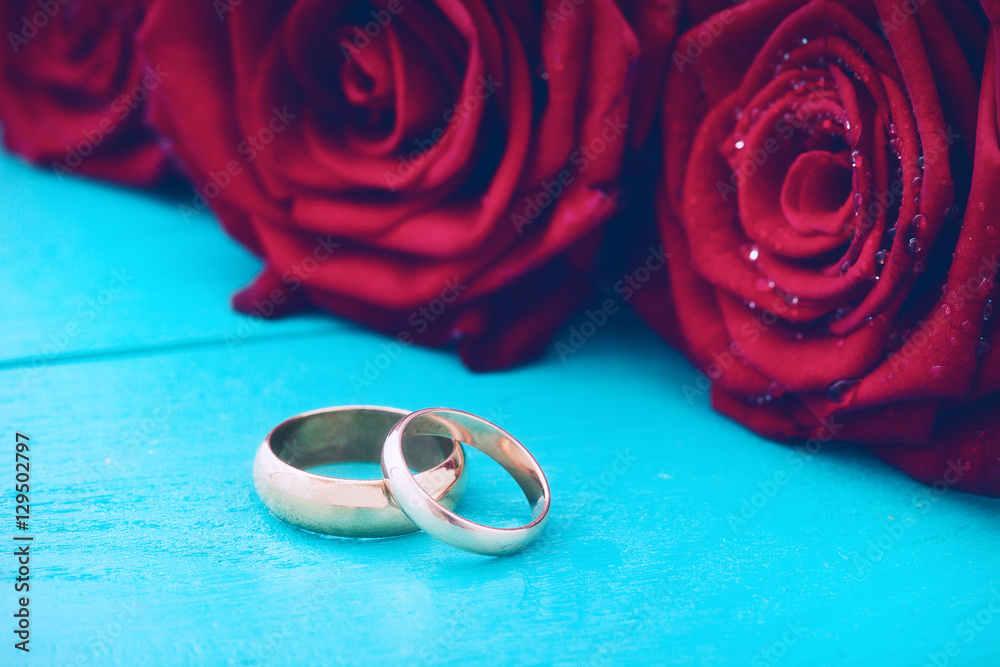 Wedding rings and red roses. Wedding bouquet on blue wooden background. Selective focus. Copy space and mock up