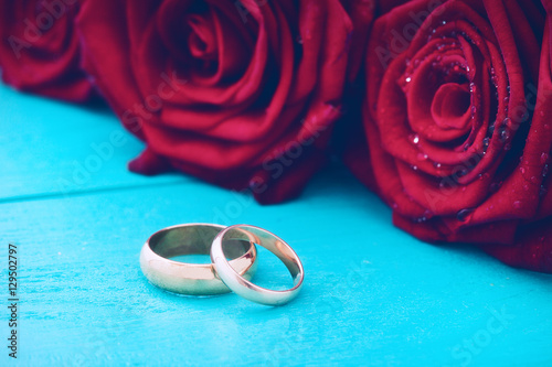 Wedding rings and red roses. Wedding bouquet on blue wooden background. Selective focus. Copy space and mock up