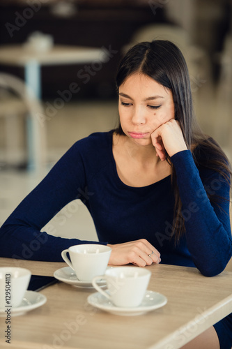 Girl sits in a cafe, props his hand on the cheek. Tired, calm expression.