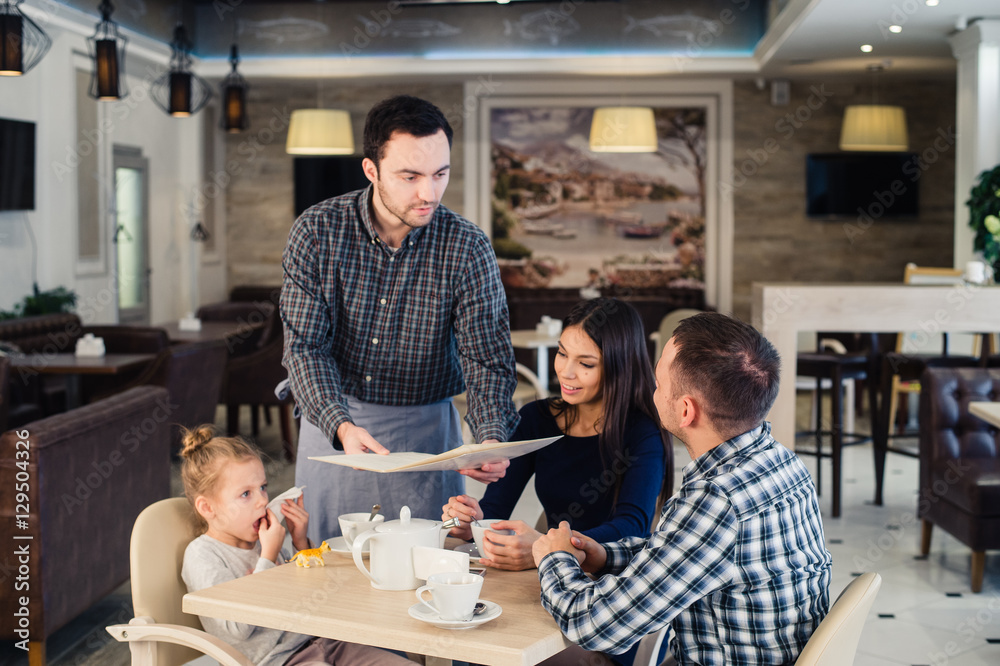 Fototapeta premium restaurant and holiday concept - waiter giving menu to happy family at cafe