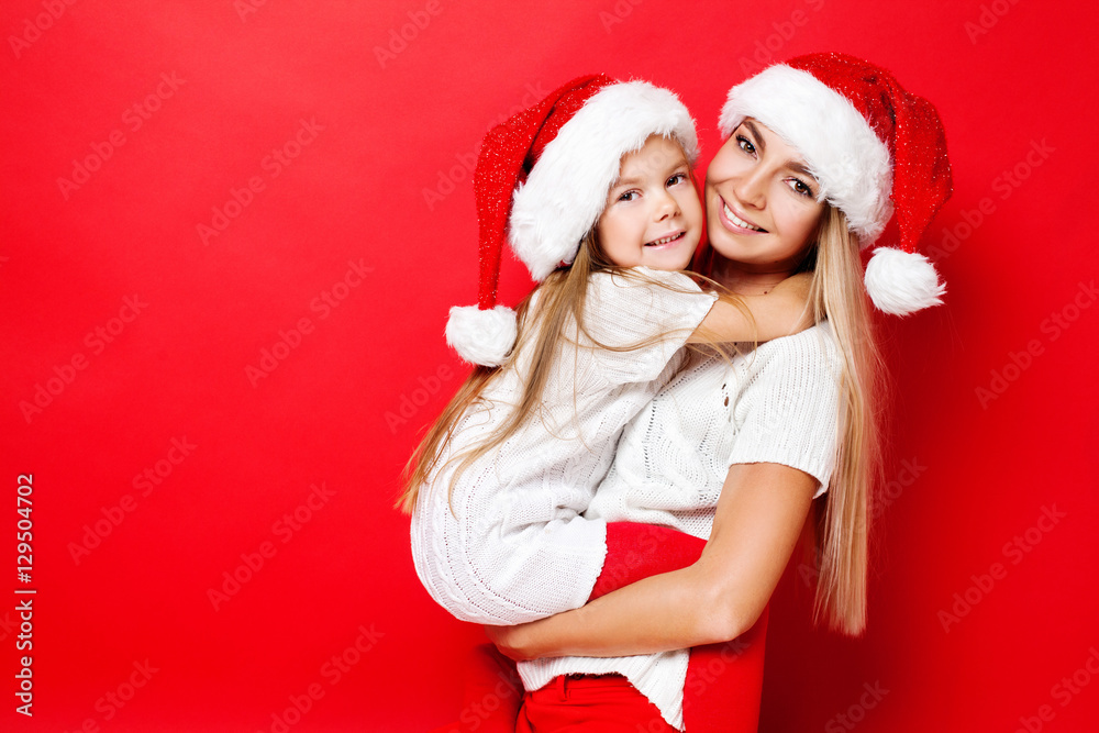 Happy mother and daughter in Christmas caps on red background. Christmas. Happy family. Happy mother and daughter in Christmas caps on red background. Christmas. Happy family.