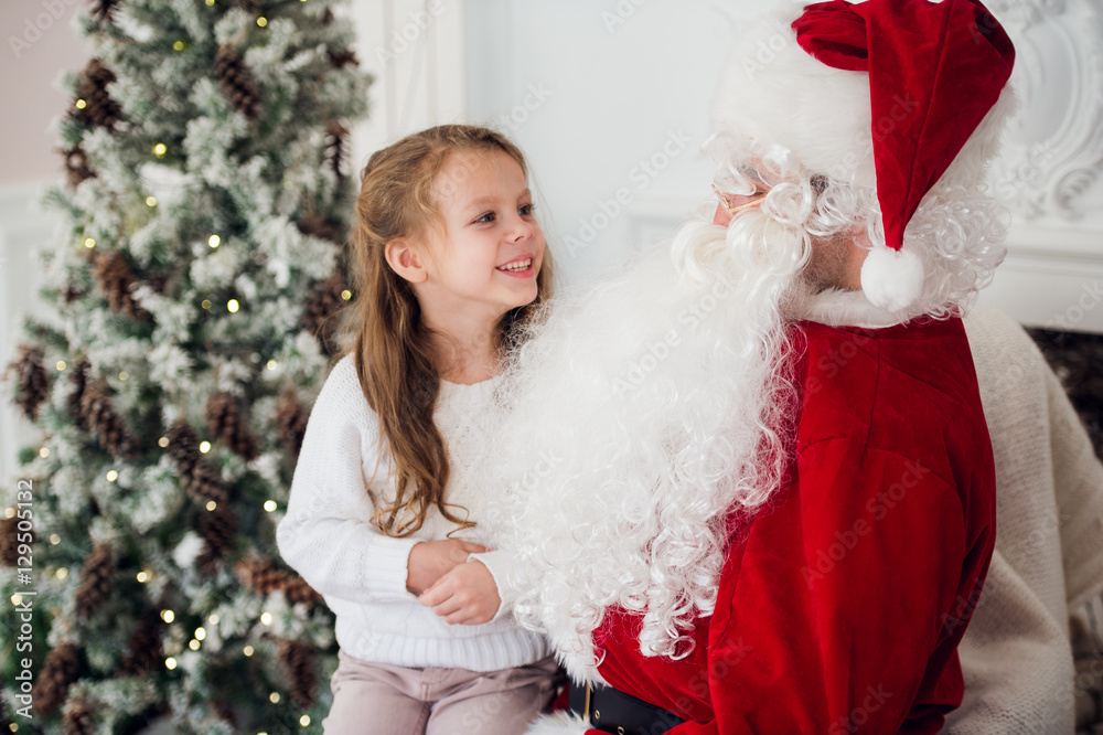 dream is real in christmastime. happy little cute girl sitting on the lap of aged Santa Claus and hugs at home near christmas tree dream is real in christmastime. happy little cute girl sitting on the lap of aged Santa Claus and hugs at home near christmas tree