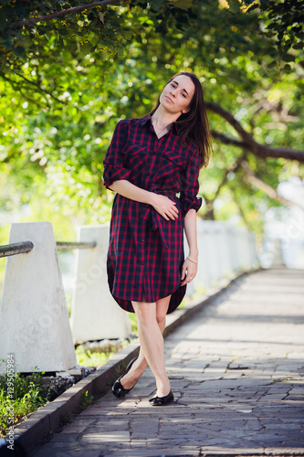 Beautiful, pretty woman in casual checkered dress walking at park outdoors. Street fashion style. photo