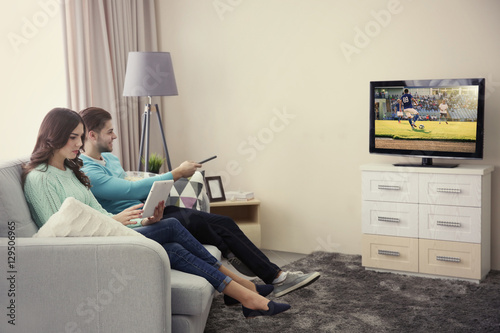 Man watching football game on television and woman using tablet at home. Leisure and entertainment concept. © Africa Studio