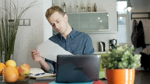 Red haired man putting bills into envelope and doing morose look to the camera
