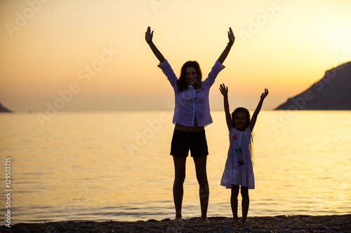 Mother and daughter lifting arms while standing on the beach at sunset