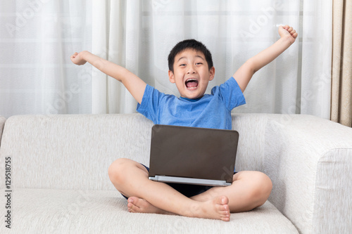 Winning Asian Chinese little boy using laptop on the sofa