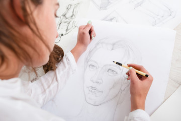Artist drawing pencil portrait close-up. Woman painter creating picture of woman on big whatman. Art, talent, craft, hobby, occupation concept