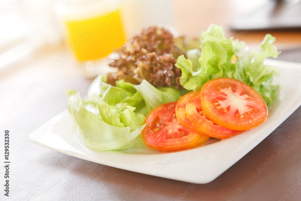 Fresh vegetable salad in white plate with orange juice background on wood table with sunlight. Fresh vegetable salad in white plate with orange juice background on wood table with sunlight.