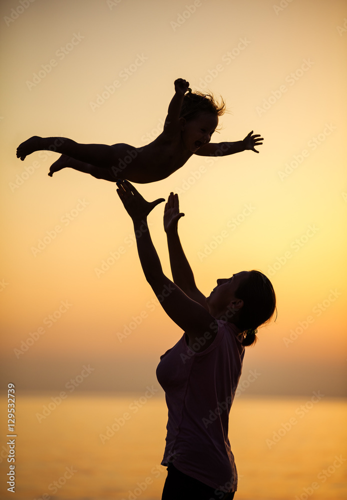 Mother and little daughter having fun on beach at sunset