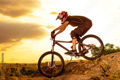 Fototapeta Naklejka Na Ścianę i Meble -  Professional Cyclist Riding the Bike Down Rocky Hill at Sunset. Extreme Sport. Space for Text.