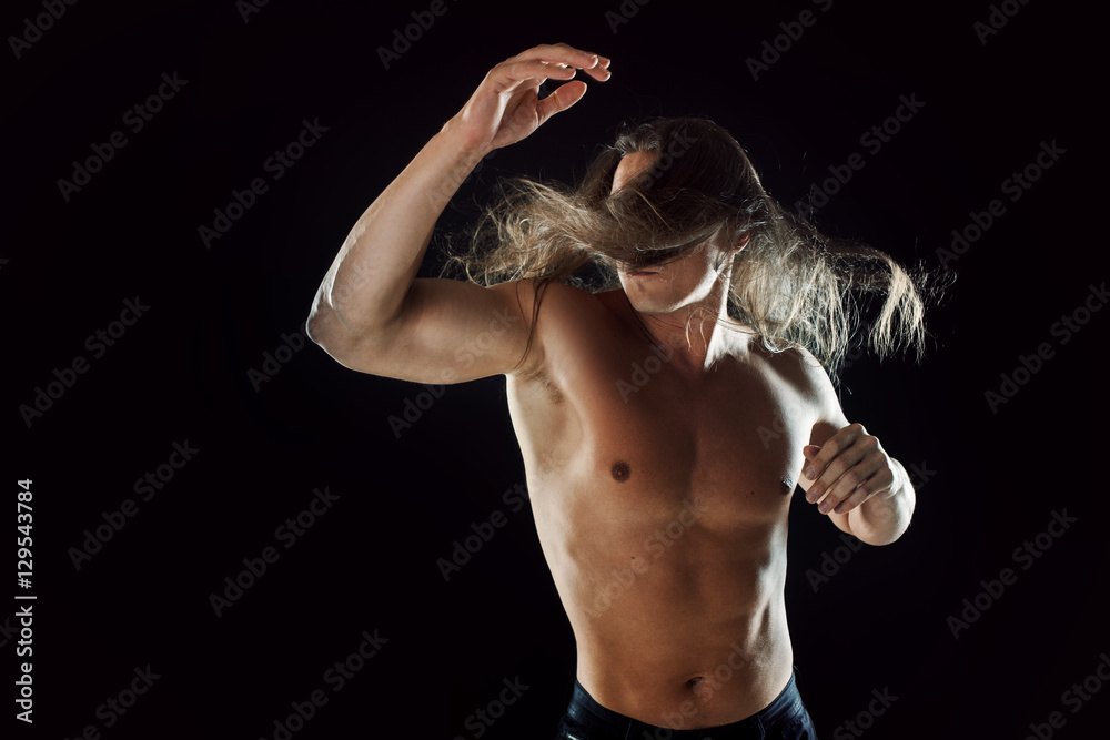 Fighting muscular man with long hair, clasps hands in fist, black background
