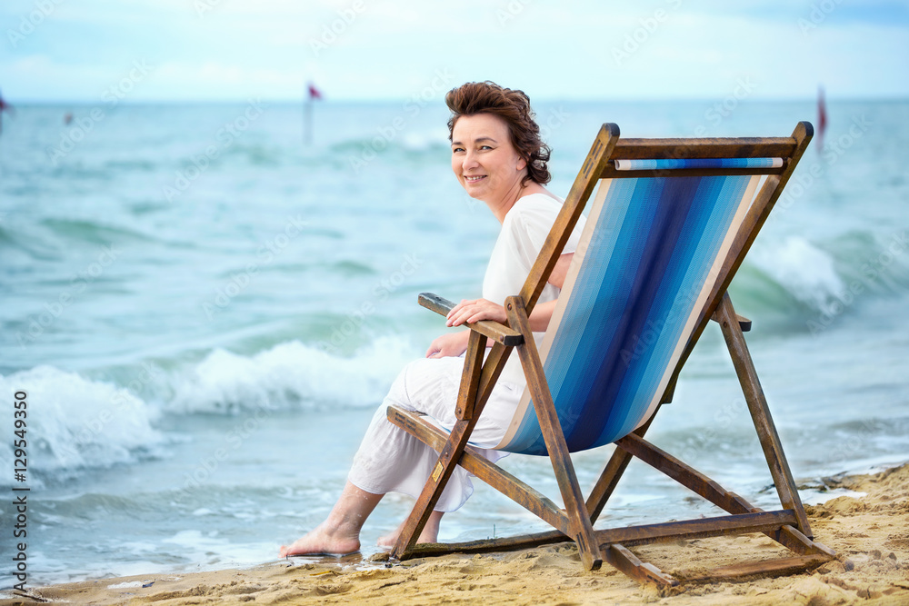 Laughing adult woman sitting in a chair on the beach and looking