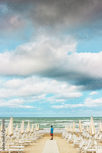 Lonely man is standing on the empty beach and looking out to the © ansyvan