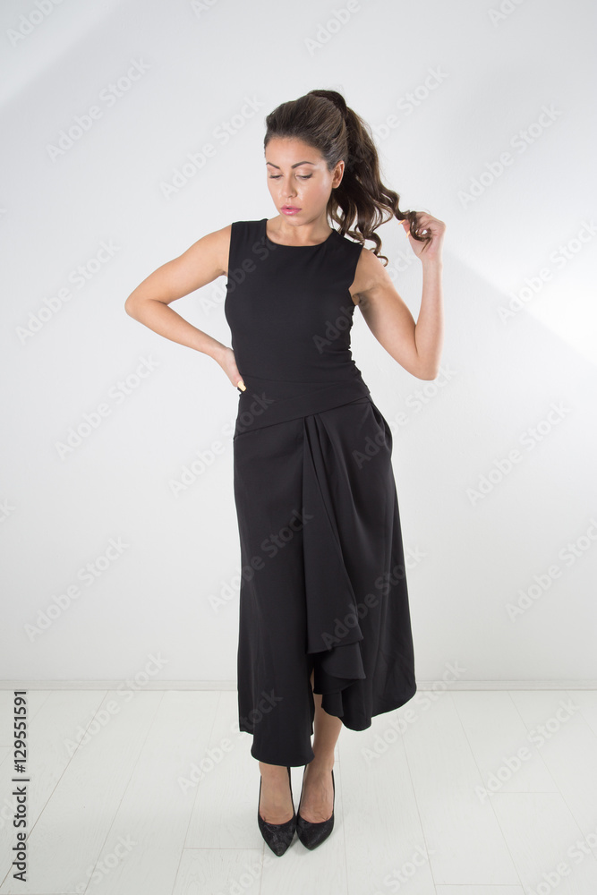Fashion Woman Posing In Black Elegant Dress Touching Her Hair And Looking Down, Full-Length Studio Shot Over White Background Fashion Woman Posing In Black Elegant Dress Touching Her Hair And Looking Down, Full-Length Studio Shot Over White Background