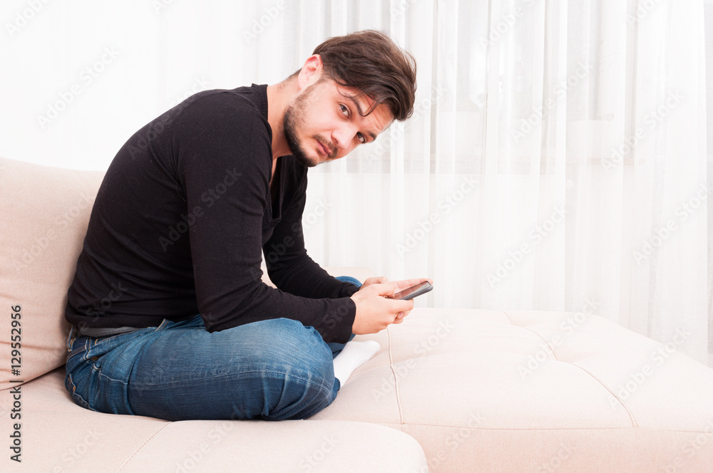 Man sitting on sofa holding smartphone and texting