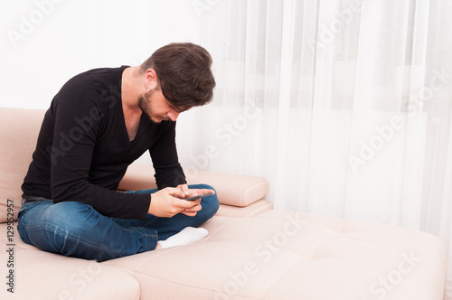 Man sitting on sofa holding smartphone and texting