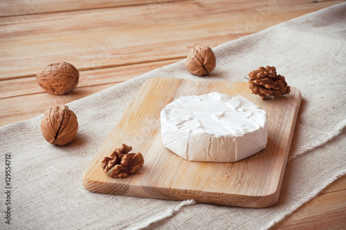Sliced round camembert cheese on a wooden board with nuts. Rustic style and natural light. Top view. Vintage burlap napkin background. 