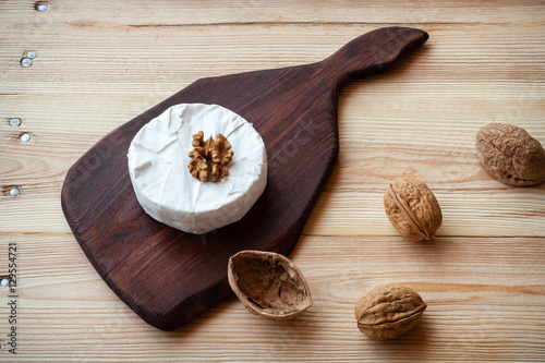 Fototapeta Naklejka Na Ścianę i Meble -  Sliced round camembert cheese on a wooden board with nuts. Rustic style and natural light. Top view. Vintage burlap napkin background.
