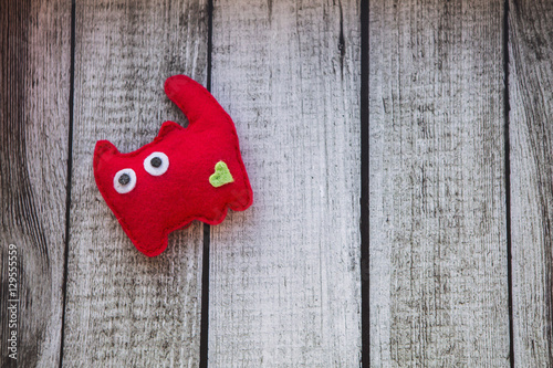красный кот игрушка из фетра с зеленым сердечком на сером деревянном столе