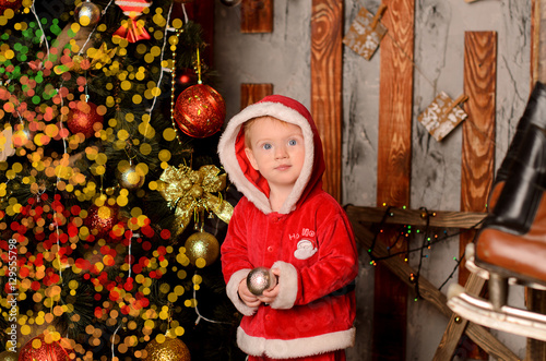 pretty child in a suit of Santa Claus  near Christmas tree photo