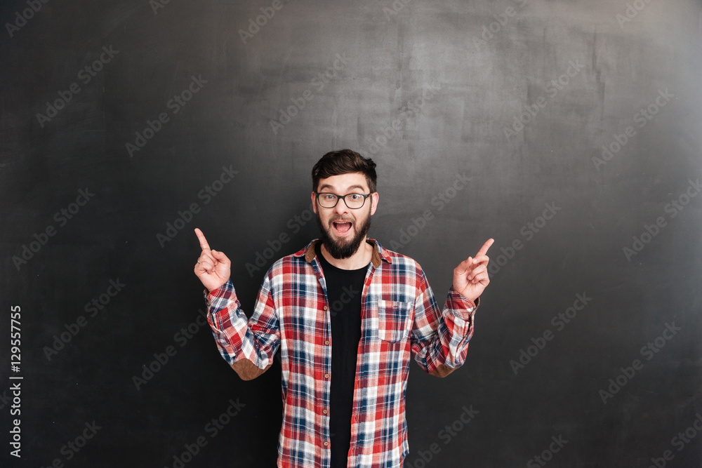 Happy young man in glasses pointing away with both hands