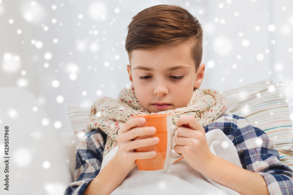 ill boy with flu in scarf drinking tea at home ill boy with flu in scarf drinking tea at home