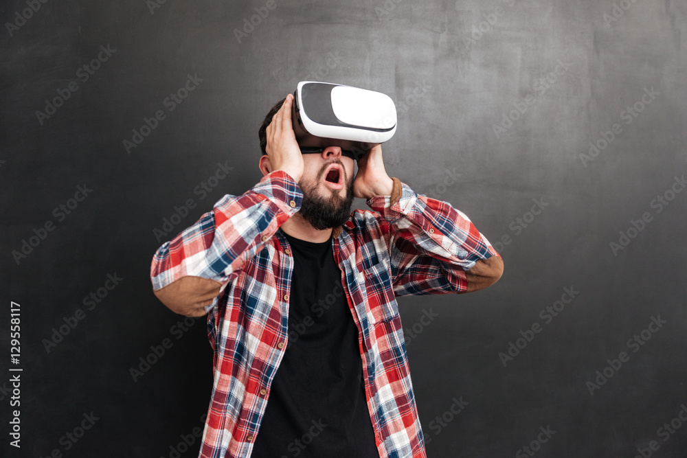 Shocked man wearing virtual reality device standing over chalkboard Shocked man wearing virtual reality device standing over chalkboard