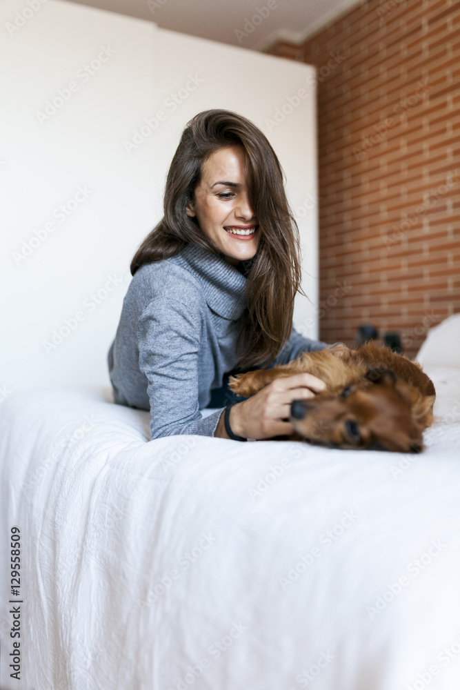 Happy young woman lying in bed playing with her dog Happy young woman lying in bed playing with her dog