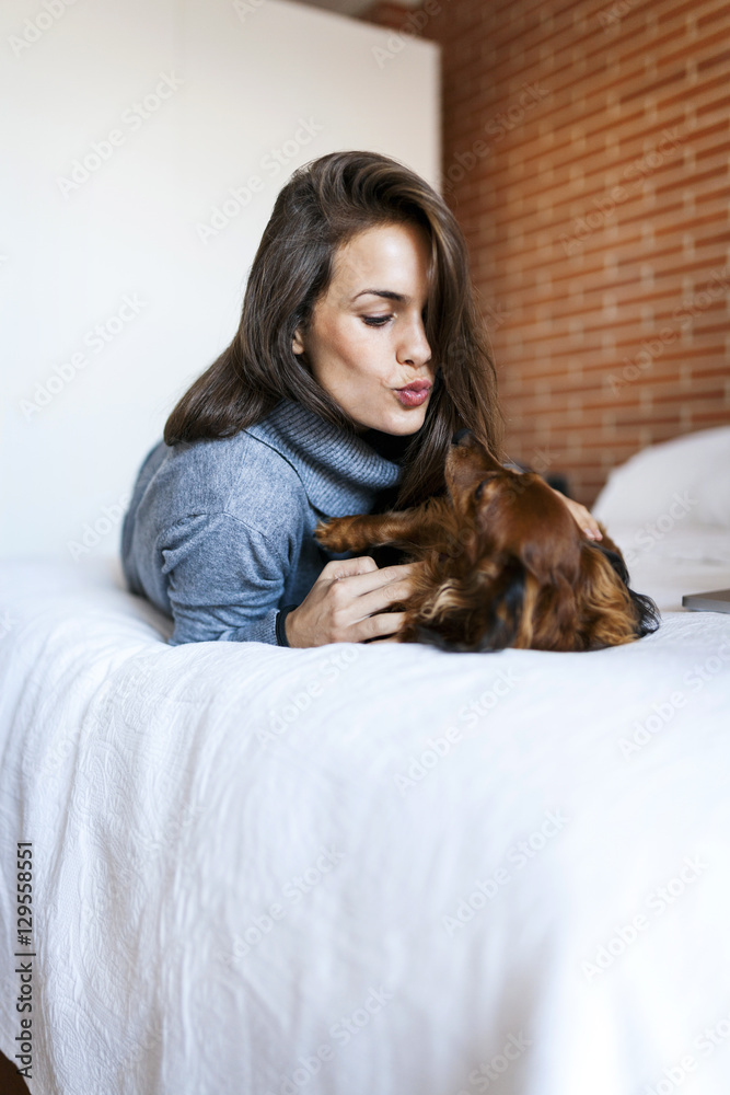 Young woman lying in bed playing with her dog Young woman lying in bed playing with her dog