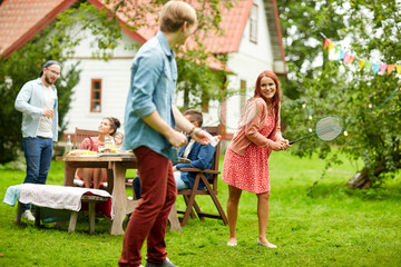 happy friends playing badminton at summer garden