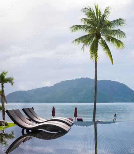 Nice pool with sun deck outdoors on bright summer day and coconut tree on the beach