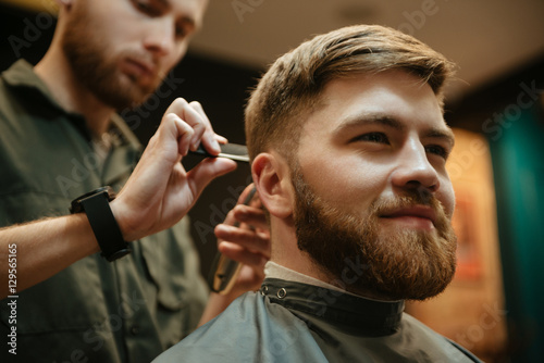 Image of cheerful man getting haircut by hairdresser in barbershop