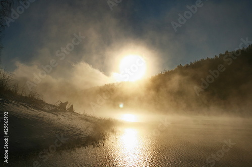 Winter landscape. Foggy winter sunset, colorful winter evening, bright sunshine over a river