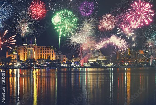 Night panoramic view of Eilat with festive fireworks. Red Sea coast. Israel. Seaside with water sparkle reflection.Embankment. Hotels. Travel,vacation and holidays theme.Toned colors