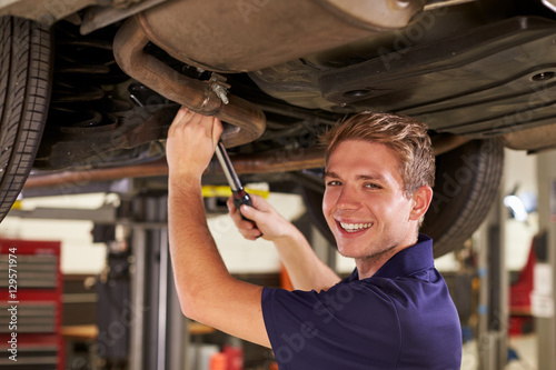 Fotografie Portrait Of Auto Mechanic Working Underneath Car In Garage