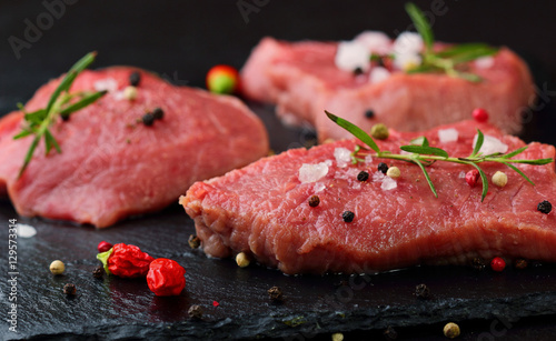 Fresh Raw Beef steak Mignon, with salt, peppercorns, rosemary, pepepr chili.On dark table.Copy space.Selective focus